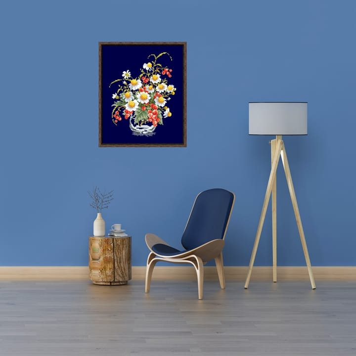 Framed chamomile cross stitch on a blue wall beside a chair and a lamp