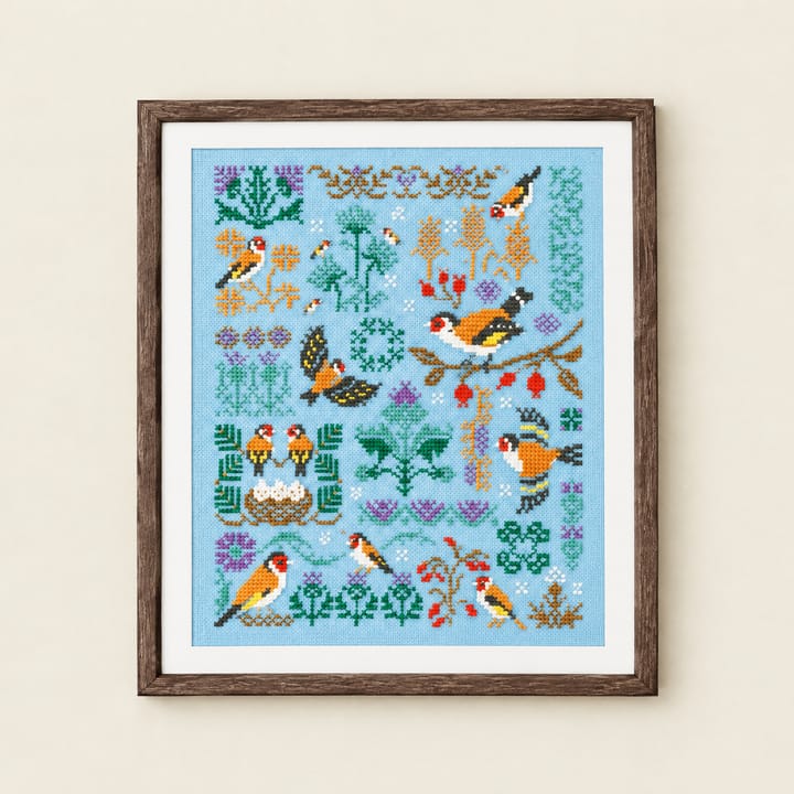Framed goldfinch sampler cross stitch above a small sideboard